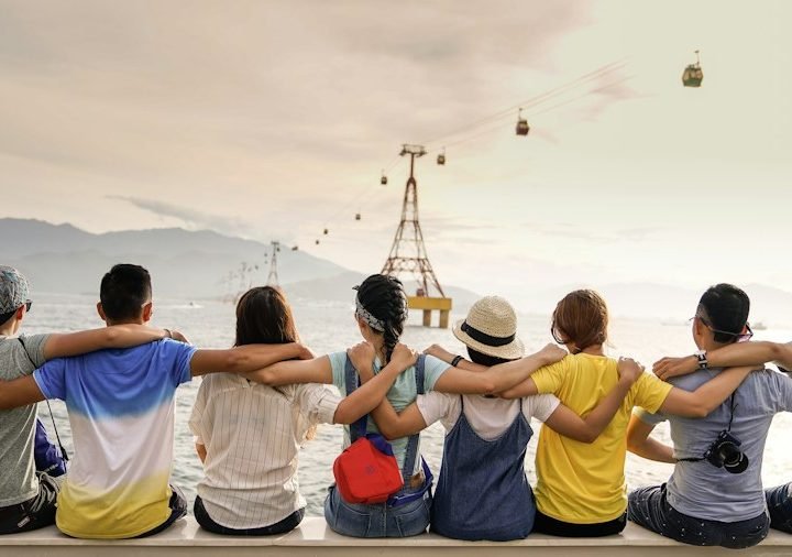 Row of friends sitting arm in arm, looking out at the view on a road trip