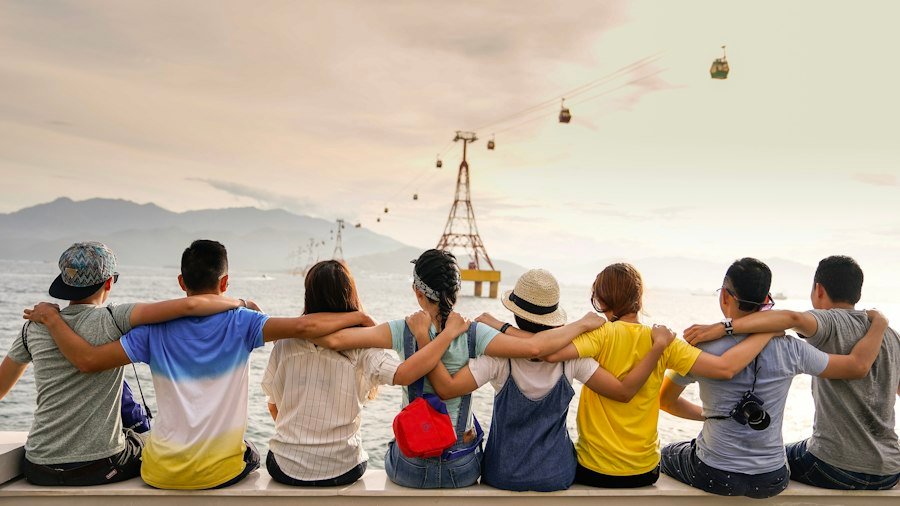 Row of friends sitting arm in arm, looking out at the view on a road trip