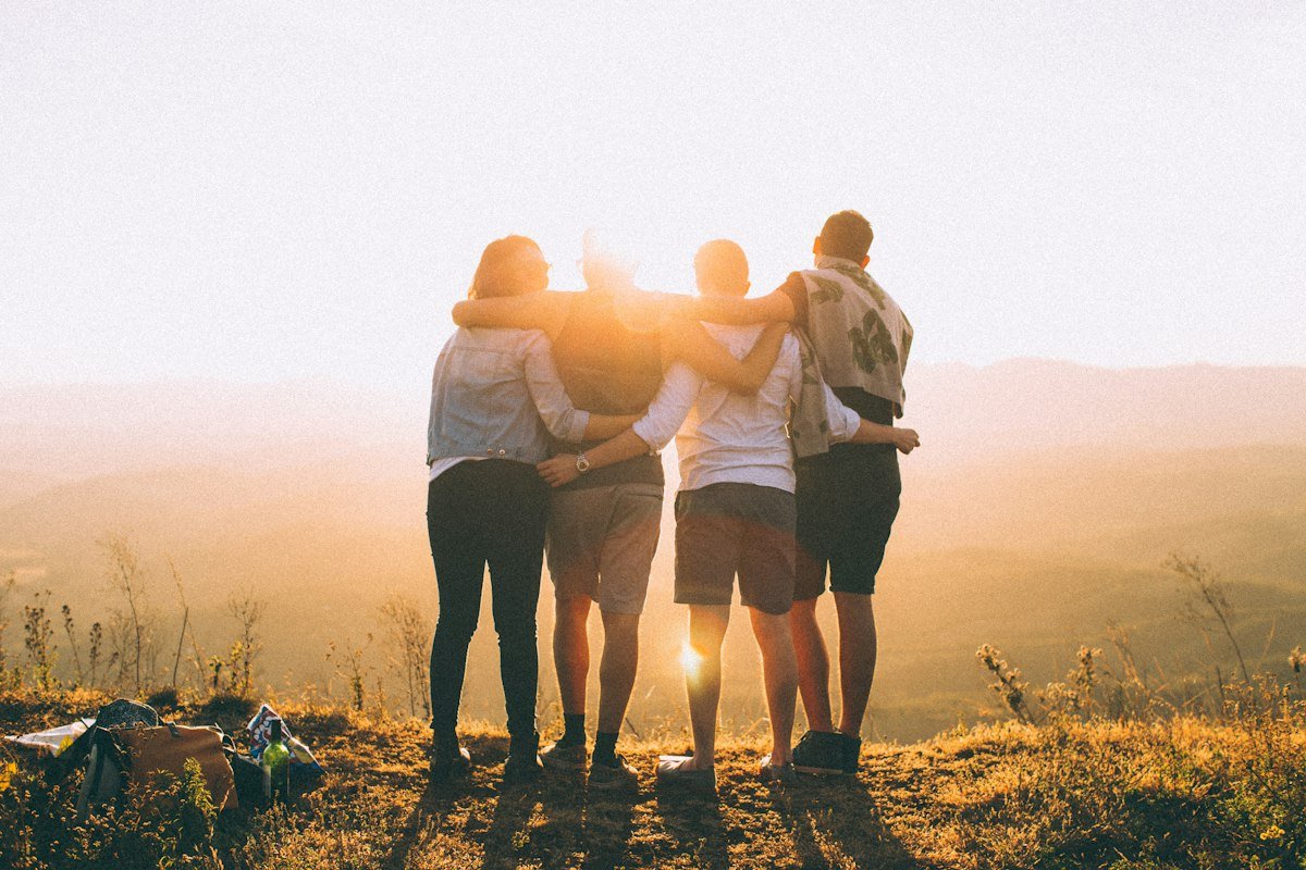 Group of friends with arms around each other watching the sunset on a hill